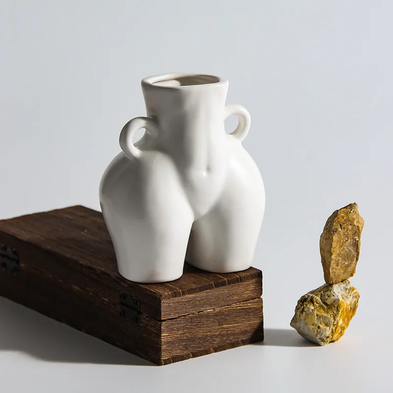 White ceramic human form vase on a wooden box