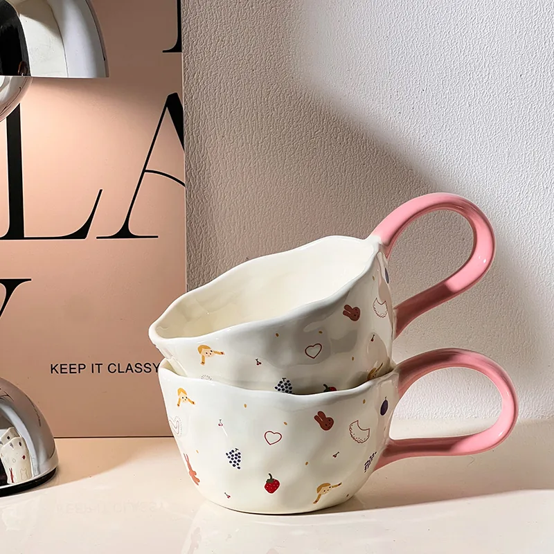 Stacked white ceramic mugs with pink handles and playful illustrations