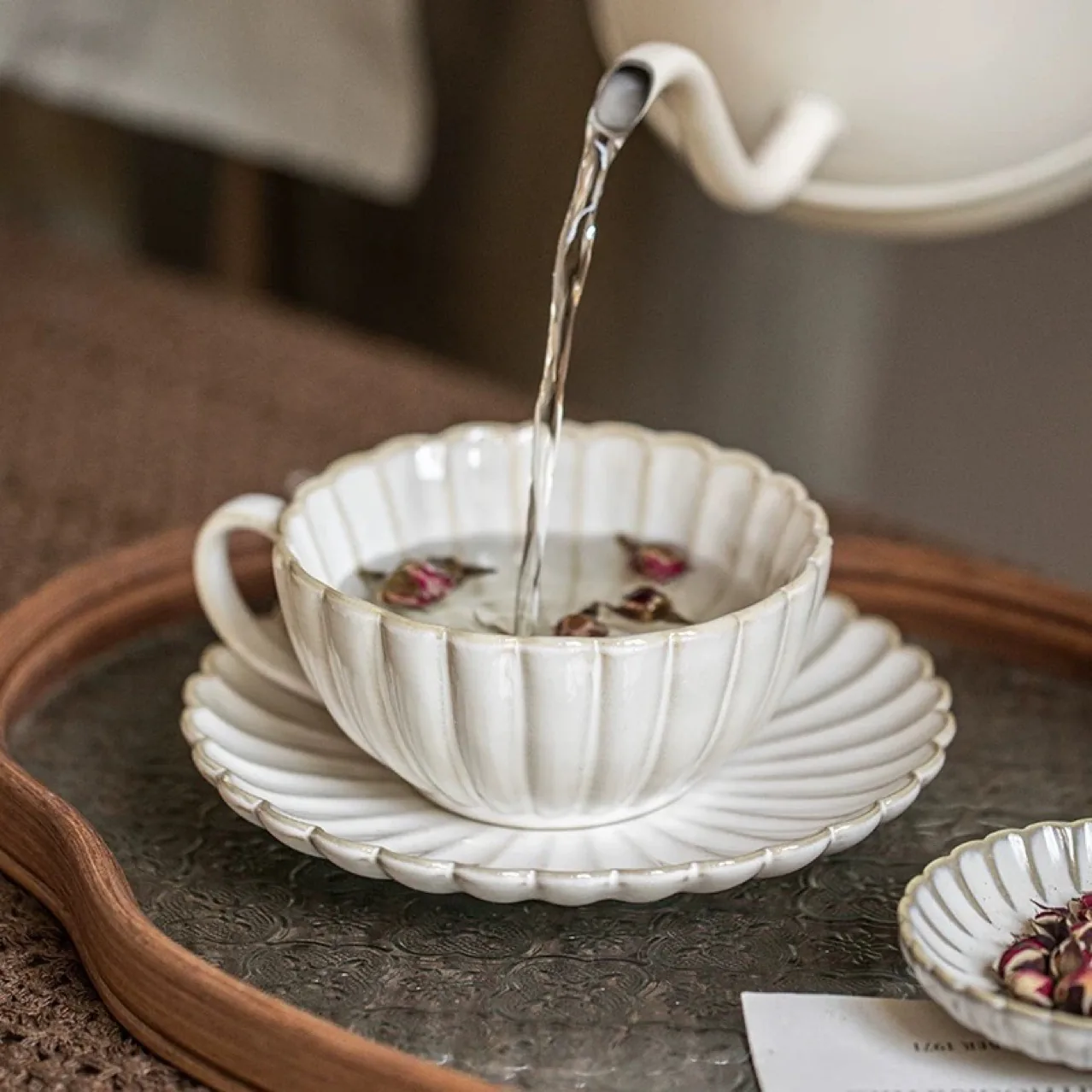 Tea being poured into petal-shaped ceramic cup and saucer